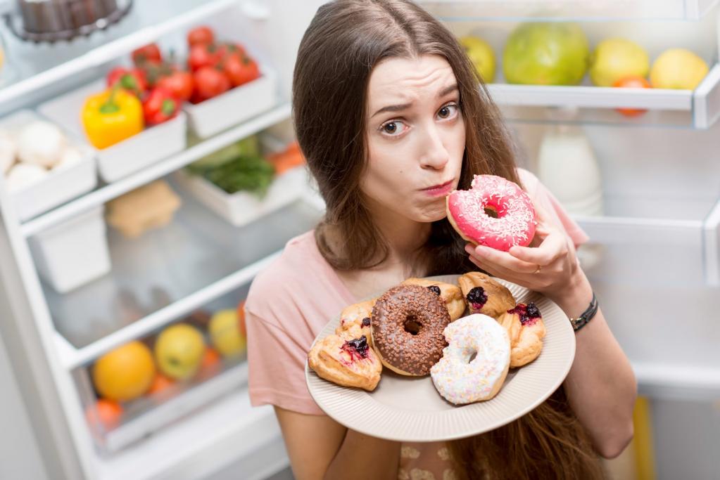 Девушка ест перед холодильником